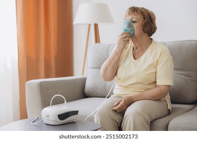 Sick senior woman has a viral infection or flu, labored breathing, asthma. An elderly female is using inhaler, nebulizer for self treatment sitting alone on the sofa at home - Powered by Shutterstock