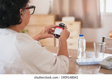 Sick senior woman hold pills bottle and read medicine prescription label and looking at medicine instructions side effects at home. Health and Medical concept. - Powered by Shutterstock