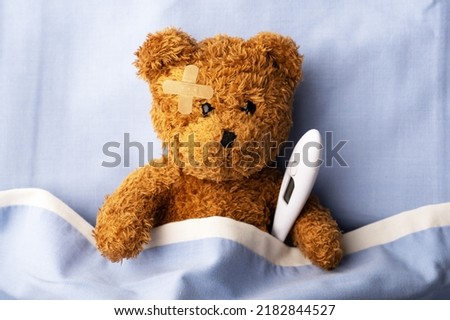 Sick teddy bear on hospital bed with thermometer and plaster patch on head. Pediatrical and child medicine concept