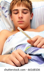 Sick Teenager Laying In Bed With Focus On Thermometer