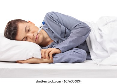 Sick Teenager With A Thermometer In His Mouth Lying In Bed Isolated On White Background