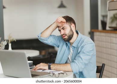 Sick Tired Exhausted Young Man Sitting Alone At Table In Coffee Shop Cafe Restaurant Indoor Working Or Studying On Laptop Pc Computer Put Hand On Head. Freelance Mobile Office Business Concept