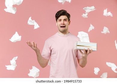 Sick unhealthy ill allergic man has red watery eyes runny stuffy sore nose suffer from allergy trigger symptoms hay fever hold paper napkin handkerchief isolated on pastel pink color background studio