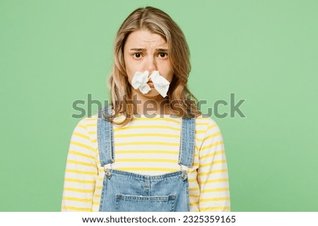 Sick unhealthy ill allergic woman has red watery eyes runny stuffy sore nose suffer from allergy trigger symptoms hay fever close nose with napkin isolated on plain green background studio portrait