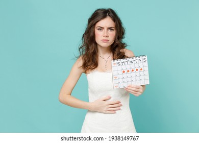 Sick upset bride woman in white wedding dress hold female periods calendar for checking menstruation days put hand on stomach isolated on blue turquoise background. Ceremony celebration party concept
