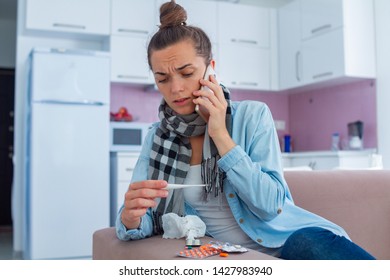 Sick Upset Woman Looking On A Medical Thermometer And Calling Family Doctor Home. Cold Treatment At Home. High Fever During Flu