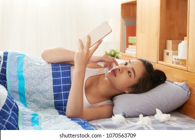 Sick Vietnamese Woman Lying In Bed And Reading News In Her Phone