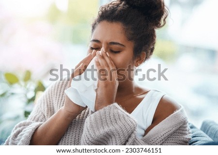 Sick, virus and a woman blowing nose on the sofa with covid, hay fever or allergies in a house. Flu, young lady and an allergy, sinus problem or sneezing into a tissue on the living room couch