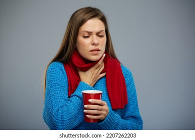 Sick woman with cold fever touching her neck, sore throat, holding red mug. Female person isolated portrait, looking away down.