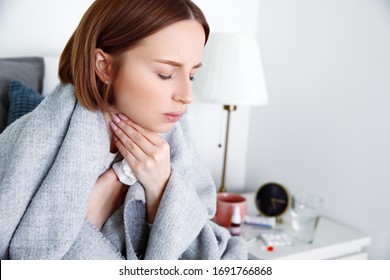 Sick woman covered in blanket at home in isolation at quarantine suffering from throat pain. Lymph glands, painful swallowing, pharyngitis, laryngeal swelling. First symptoms of covid-19 coronavirus