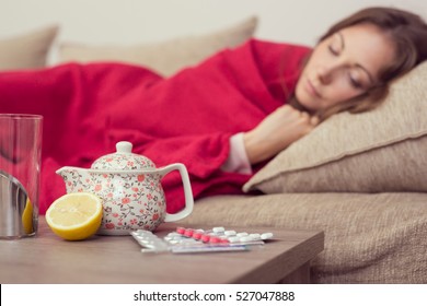 Sick woman covered with a blanket lying in bed with high fever and a flu, resting. Teapot, pills and lemon on the table, focus on the teapot - Powered by Shutterstock