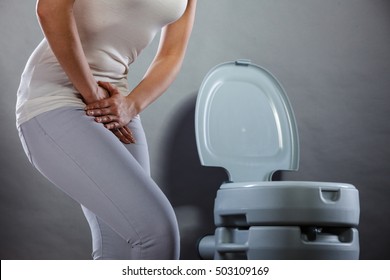 Sick woman with hands holding pressing her crotch lower abdomen in front of toilet bowl. Medical problems, incontinence, health care concept