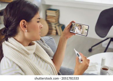 Sick woman having online medical consultation video call. Coughing young girl with bad cold, flu or Covid 19 fever holding thermometer and looking at telemedicine service doctor on mobile phone screen