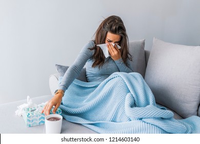 Sick woman with headache sitting under the blanket. Sick woman with seasonal infections, flu, allergy lying in bed. Sick woman covered with a blanket lying in bed with high fever and a flu, resting. 