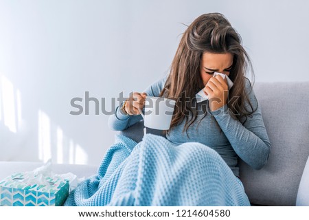 Sick woman with headache sitting under the blanket. Sick woman with seasonal infections, flu, allergy lying in bed. Sick woman covered with a blanket lying in bed with high fever and a flu, resting. 