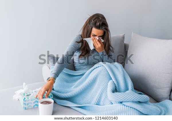 Sick woman with headache sitting under the blanket. Sick\
woman with seasonal infections, flu, allergy lying in bed. Sick\
woman covered with a blanket lying in bed with high fever and a\
flu, resting. 