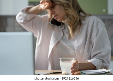 Sick Woman Holding Sparkling Water Glass With Dissolving Effervescent Aspirin Pill, Talking On Cellphone, Taking Painkiller To Relieve Headache Or Fever, Focus On Foreground. Female Taking Medication