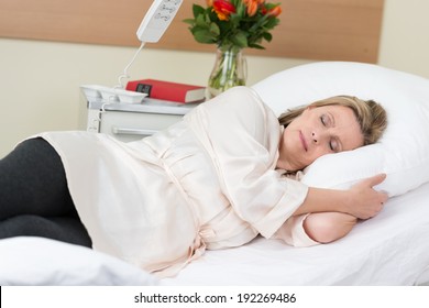 Sick woman in hospital lying sleeping on a hospital bed with a peaceful expression turned on her side facing the camera - Powered by Shutterstock