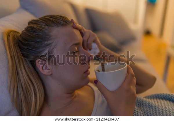 Sick woman lying on sofa. Young girl sick in\
bed with temperature drinks hot. Sick woman covered with a blanket\
lying in bed with high fever and a flu.\
