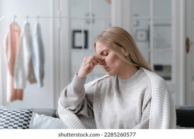 sick woman with nasal pain touching nose and feeling bad, girl with grippe and rhinitis wrapped with warm plaid and sitting upset at home alone