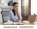 Sick woman with runny nose at table in office