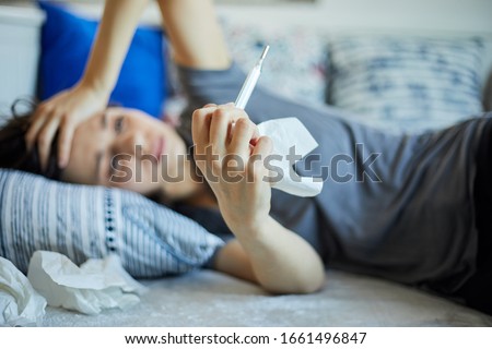 Sick woman with thermometer lying in bed with cold and high fever.