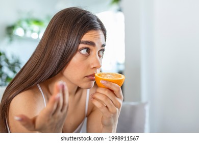 Sick woman trying to sense smell of half fresh orange, has symptoms of Covid-19, corona virus infection - loss of smell and taste. One of the main signs of the disease.