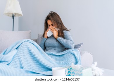 Sick Woman.Flu.Woman Caught Cold. Sneezing into Tissue. Headache. Virus .Medicines. Young Woman Infected With Cold Blowing Her Nose In Handkerchief. Sick woman with a headache sitting on a sofa  - Powered by Shutterstock