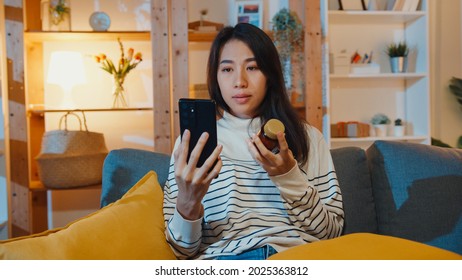 Sick Young Asian Lady Hold Medicine Sit On Couch Video Call With Phone Consult With Doctor At Home Night. Girl Take Medicine After Doctor Order, Quarantine At House, Social Distance Corona Virus.