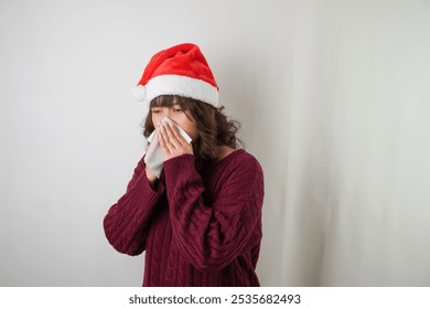 Sick young asian woman wearing santa clause hat and red long sleeved sweater is sneezing and covering using tissue, isolated over white background. Concept for Christmas Holiday and New Year Party - Powered by Shutterstock