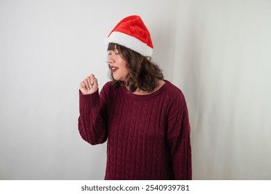 Sick young asian woman wearing santa clause hat and red long sleeved sweater is coughing and covering using hand, isolated over white background. Concept for Christmas Holiday and New Year Party - Powered by Shutterstock