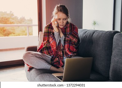 Sick Young Fair-haired Woman In Grey Sweater Covered With Plaid Sitting On Sofa With Closed Eyes, Working On PC, Talking On Phone. Illness, Work Concept