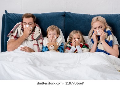 sick young family blowing noses with napkins together while lying in bed - Shutterstock ID 1187788669