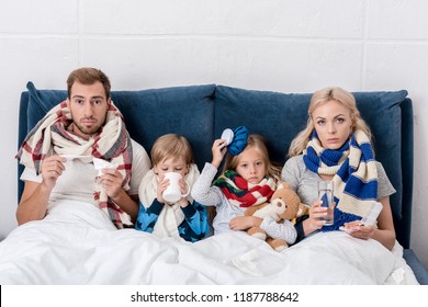 Sick Young Family Sitting In Bed Together And Looking At Camera