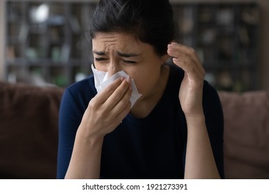 Sick young Indian woman blow in napkin suffer from runny nose having influenza or cold at home. Unhealthy ill ethnic female exhausted by flu or corona virus. Covid-19, health problem concept.