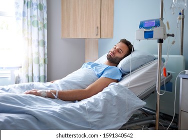 Sick Young Man Attached To An Intravenous Drip Lying On Bed In A Hospital Room 