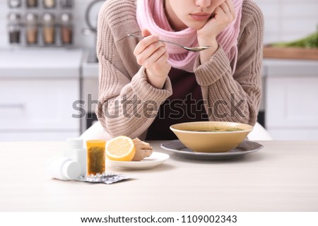 Sick young woman eating broth to cure cold at table in kitchen
