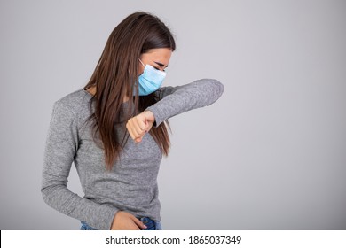 Sick Young Woman In Gray Clothes Sterile Face Mask To Safe From Coronavirus Virus Covid-19 During Pandemic Quarantine Cough In Elbow Isolated On Gray Background Studio Portrait