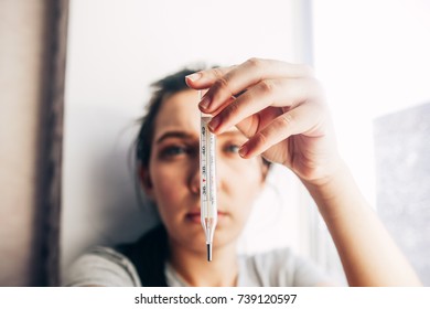 Sick Young Woman Holding A Thermometer. Blurred Background