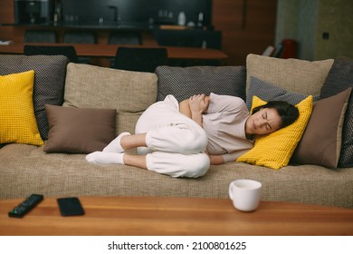 Sick Young Woman Lying On Sofa Holding On Stomach Suffering Abdominal Pain From Menstruation, Diarrhea, Or Indigestion