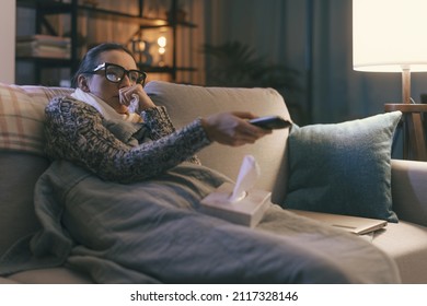 Sick young woman resting on the couch at home and watching TV, she is holding the remote control - Powered by Shutterstock