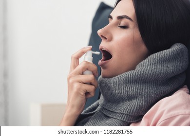 Sick Young Woman In Scarf Using Cough Spray