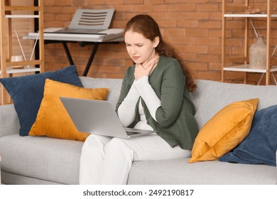 Sick young woman with sore throat and laptop sitting on sofa at home - Powered by Shutterstock