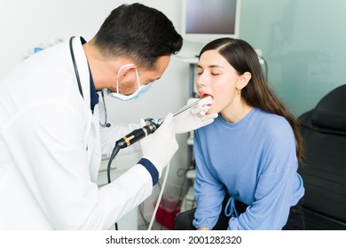 Sick Young Woman Suffering From Strep Throat Visiting The Otolaryngologist's Office. Male Doctor Using A Laparoscope To Check The Throat Of A Female Patient