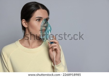 Sick young woman using nebulizer on grey background, space for text