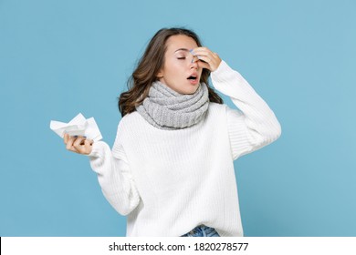 Sick young woman in white sweater scarf hold napkin put hand on nose keeping eyes closed isolated on blue background studio portrait. Healthy lifestyle ill sick disease treatment cold season concept