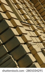 Side angle diagonal view of a historical neoclassical building facade showing textured rustic plaster blocks with geometric shadow lines.