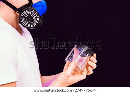 Side angle of individual in protective gear displaying empty plastic jar under purple lighting on black backdrop