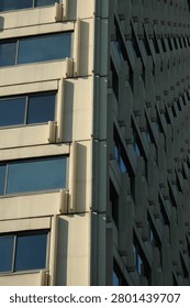 Side angle perspective view of a brutalist concrete building corner showing a repeating grid pattern of glass windows with sharp shadows.