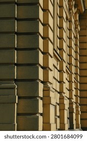 Side angle perspective view of a classical neoclassical building facade showing rhythmic rustic plaster blocks with deep geometric shadow lines.
